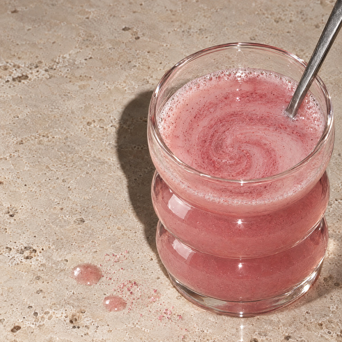 A spoon stirring the pink ALORA drink in a ribbed glass (illustrative image)