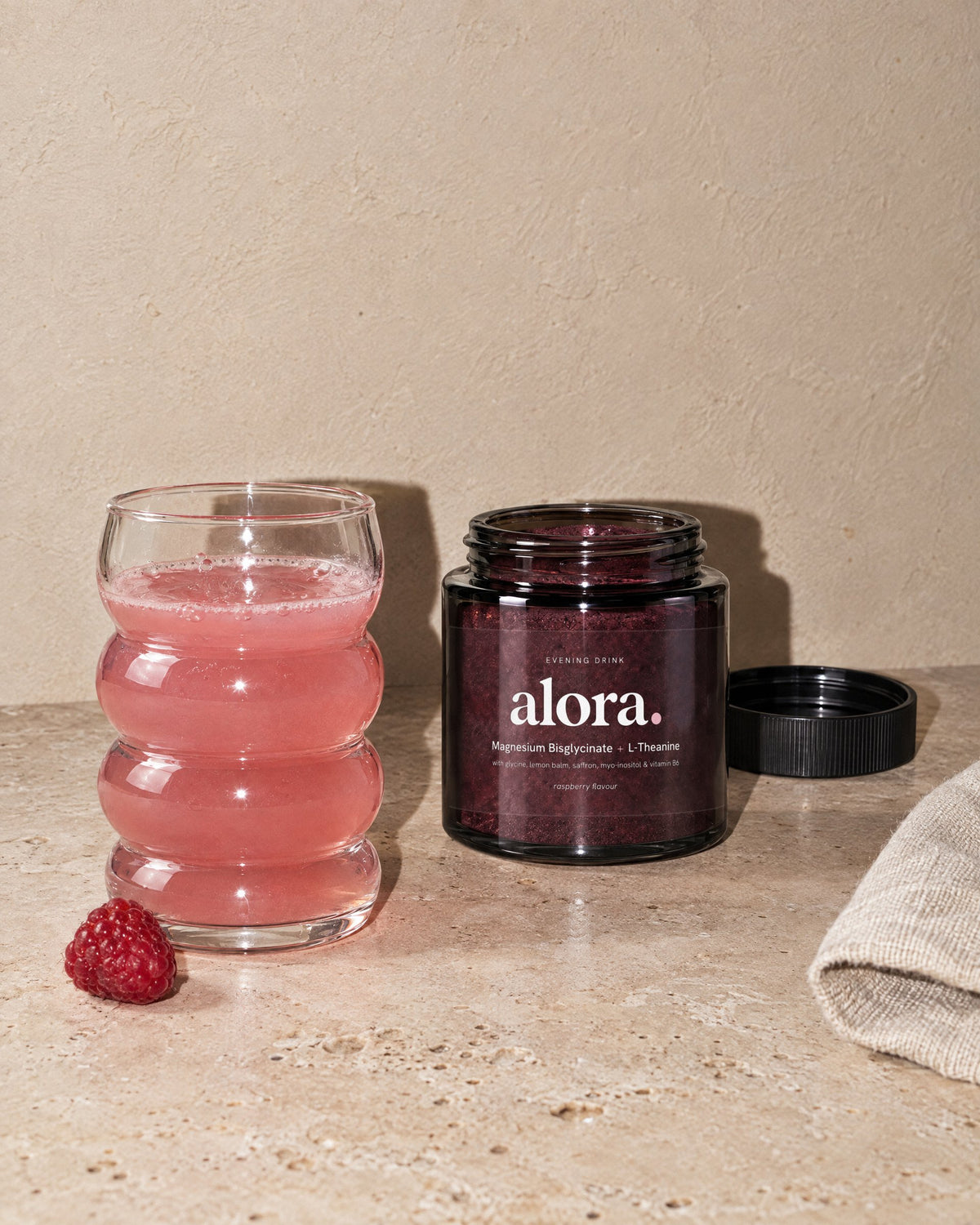 The ALORA jar with its lid off beside a glass of the drink and a raspberry (illustrative image)