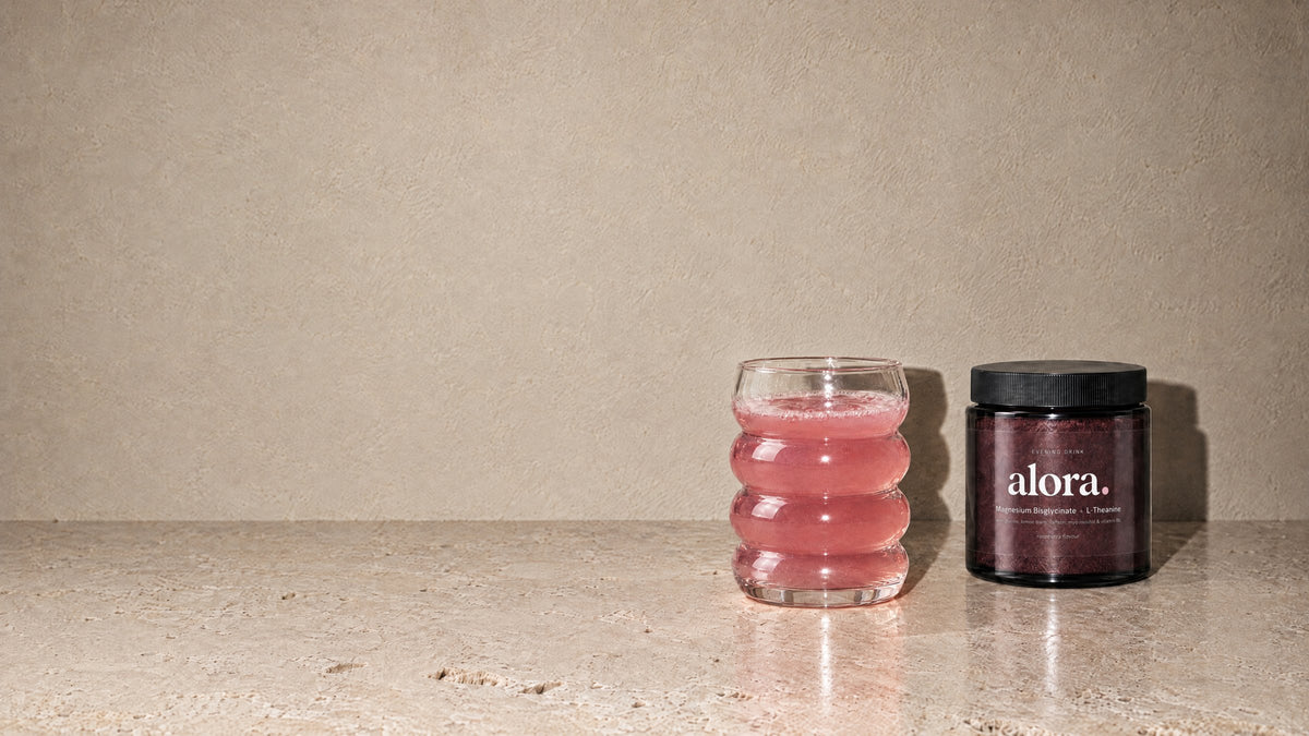 ALORA jar beside a glass of the raspberry-pink evening drink on a travertine counter (illustrative image)