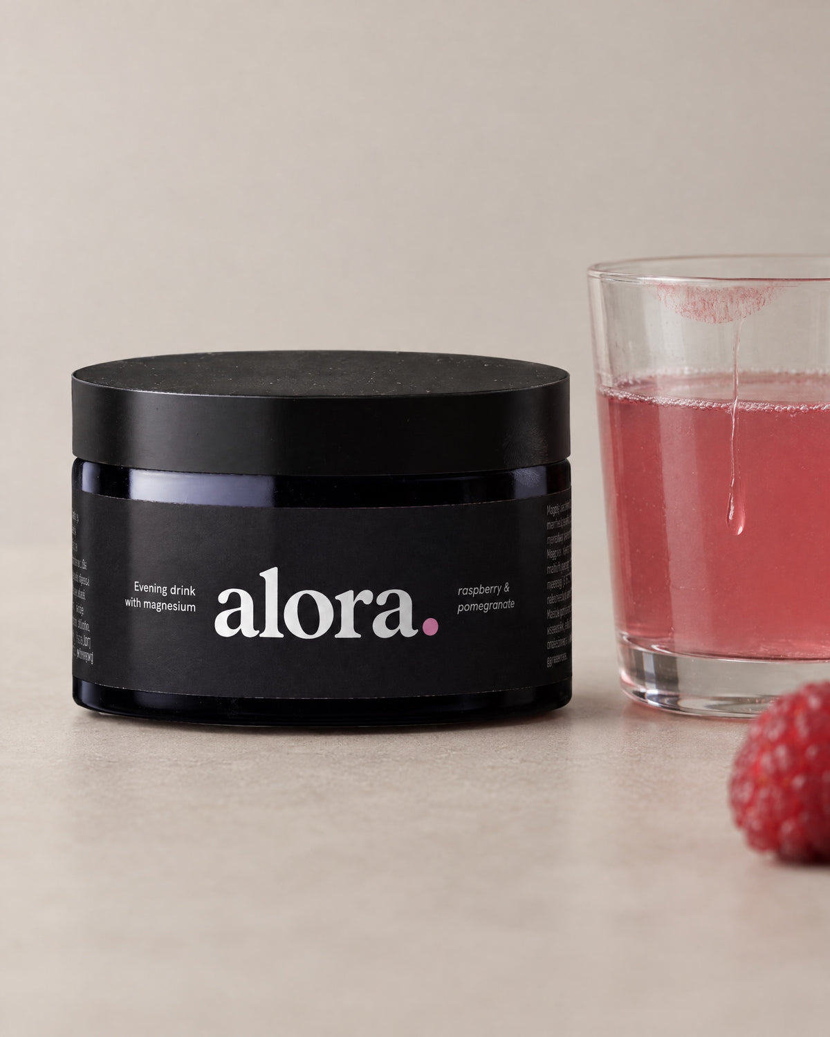 The ALORA jar next to a half-drunk glass of the raspberry-pink drink and a raspberry (illustrative image)